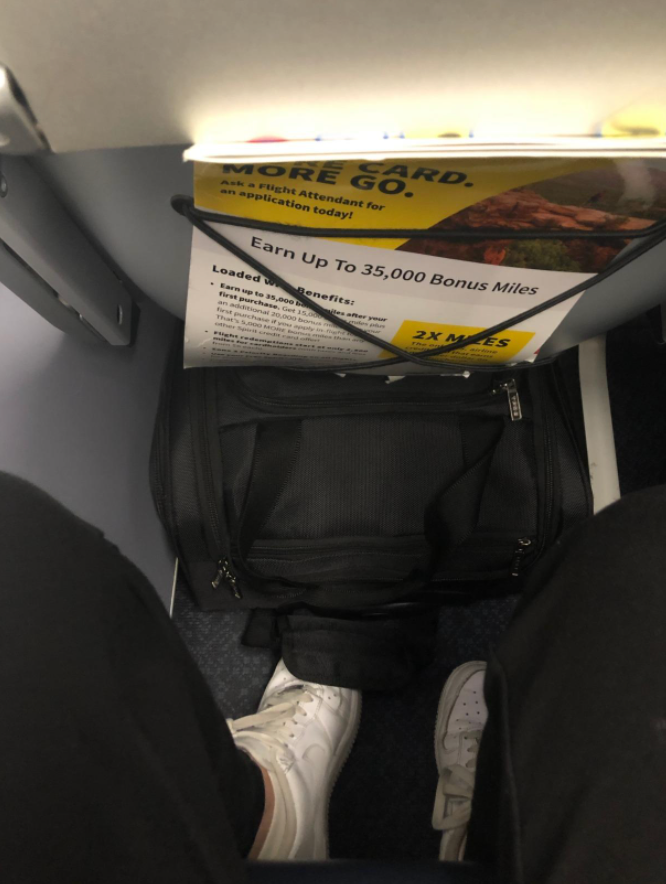 person sitting in airplane seat with wheeled suitcase fitting under seat