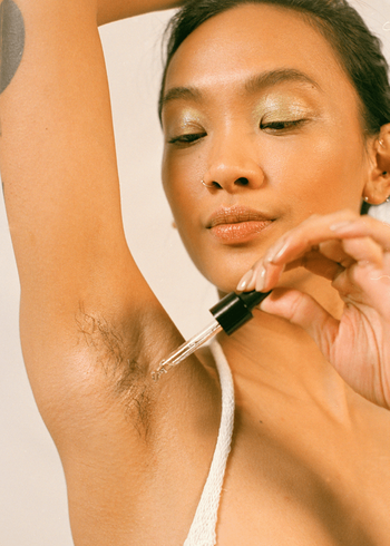 a model applying oil to their armpit using a glass dropper