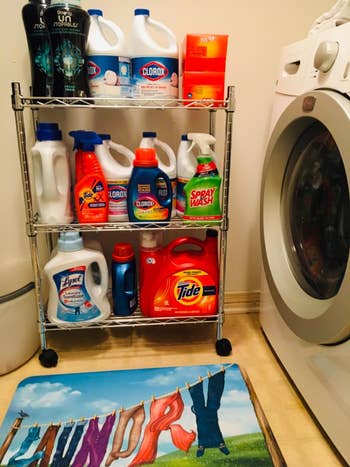 Laundry country with a washer and a support holding assorted detergent and cleaning products, including Tide and Clorox. A colorful mat lies connected the floor