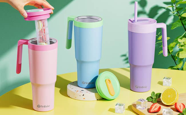 pink, blue, and purple tumblers with handles, the pink one being opened by a model showing the fruit infuser