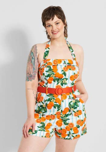 front view of model in the orange-printed romper which has a belt