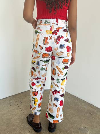 Person in patterned pants and red top, standing with back to camera, hands on hips, in a casual setting