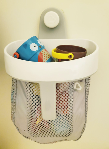 A mesh gray bag full of toys hung on a shower wall 