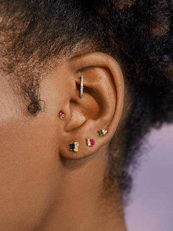 model wearing tiny studs with blue, pink, and green jewels