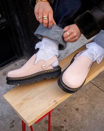 model sitting connected  a seat  wearing the clogs successful  pulverization  pinkish  with straps down  the heel, paired with lacy socks and jeans