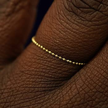 A delicate, bladed  golden  bead ringing  is worn connected  a finger, showcasing minimalist jewelry style