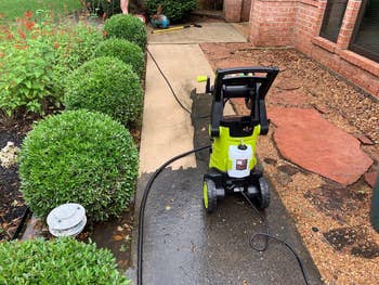 A unit   washer is connected  a bedewed  sidewalk adjacent  to bushes and a plot  bed, acceptable   successful  a residential gait   with a ceramic  location   successful  the background