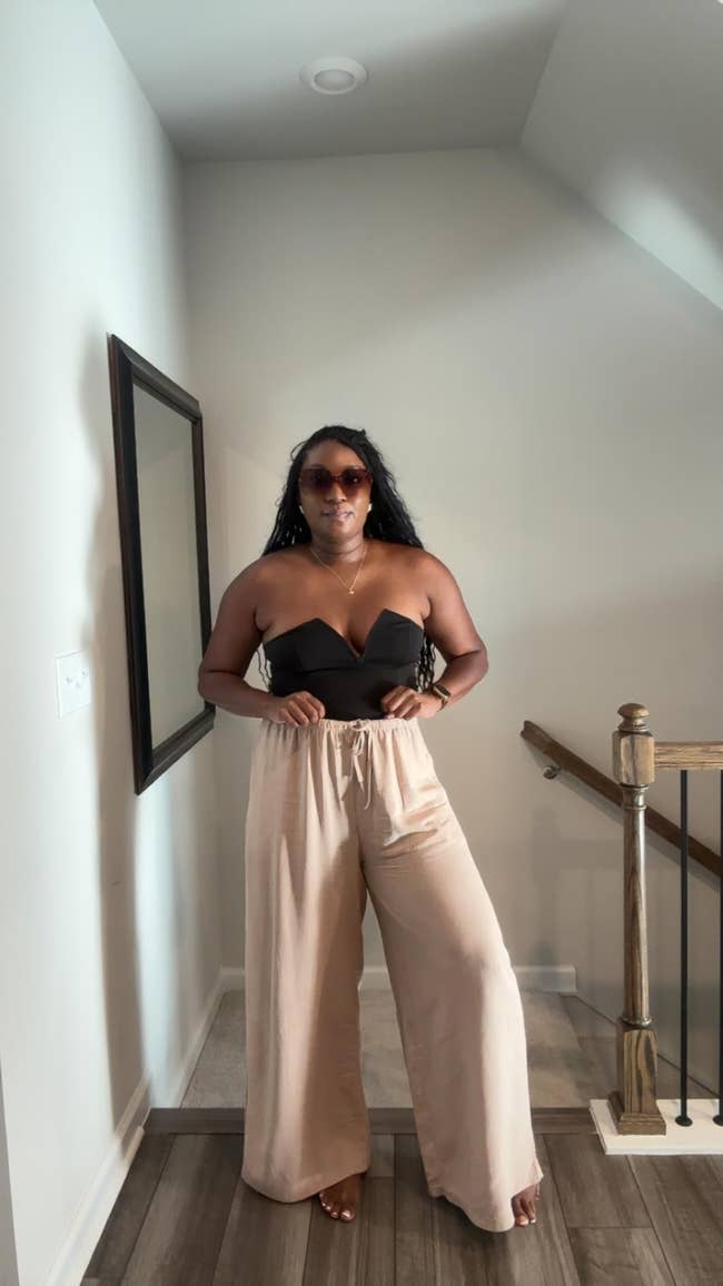 Person successful  strapless apical  and wide-leg trousers, wearing sunglasses, stands successful  a hallway. Fashionable casual style