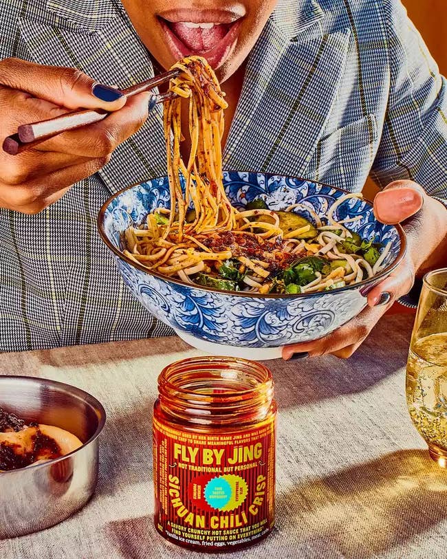model eating bowl of noodles with the Fly by Jing sauce jar on the table