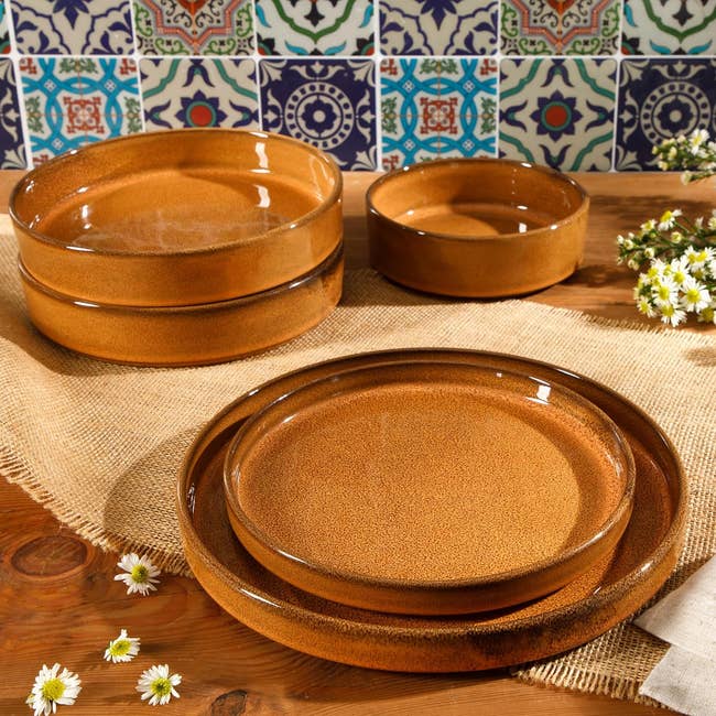 Rustic brownish stoneware dishes and bowls connected a woody array with decorative tile and tiny achromatic flowers successful the background