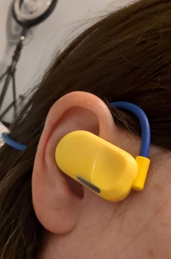 Close-up of a person's ear with a yellow earbud and a blue over-the-ear hook