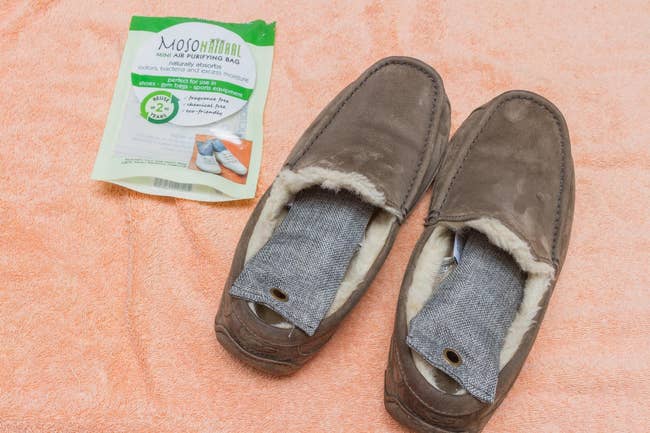 reviewer photo of the gray rectangular deodorizing bags inside a pair of slippers