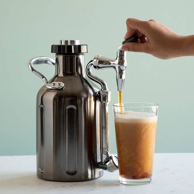 Stainless steel cold brew maker with curved spout and person pouring some out
