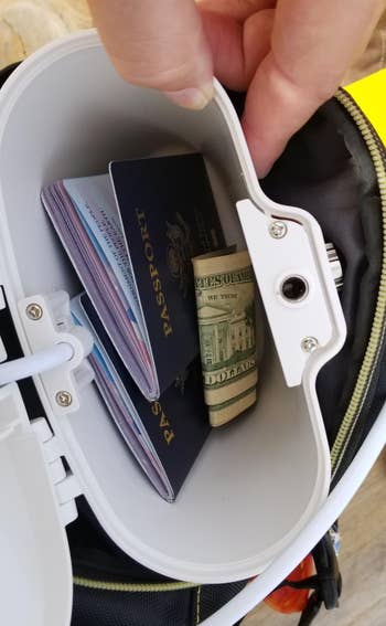 reviewer showing the inside of a white lock box, which is holding cash and passports