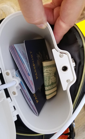 reviewer showing the inside of a white lock box, which is holding cash and passports