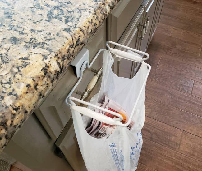 Plastic bag organizer attached to a kitchen cabinet, holding several folded plastic bags for convenient storage