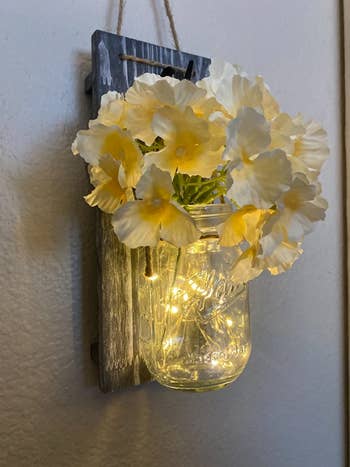 reviewer photo of one lit mason jar wall sconce hanging on a wall