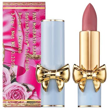 Lipstick with gold bow detail beside its packaging featuring floral design; part of Pat McGrath Labs collection