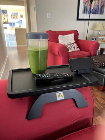 The tray in black on a reviewer's couch with a green smoothie, remote, and their cell phone on it