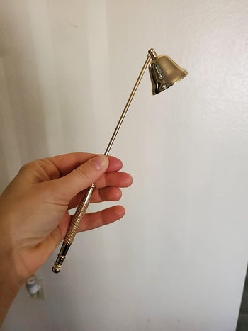 a hand holding the gold candle snuffer