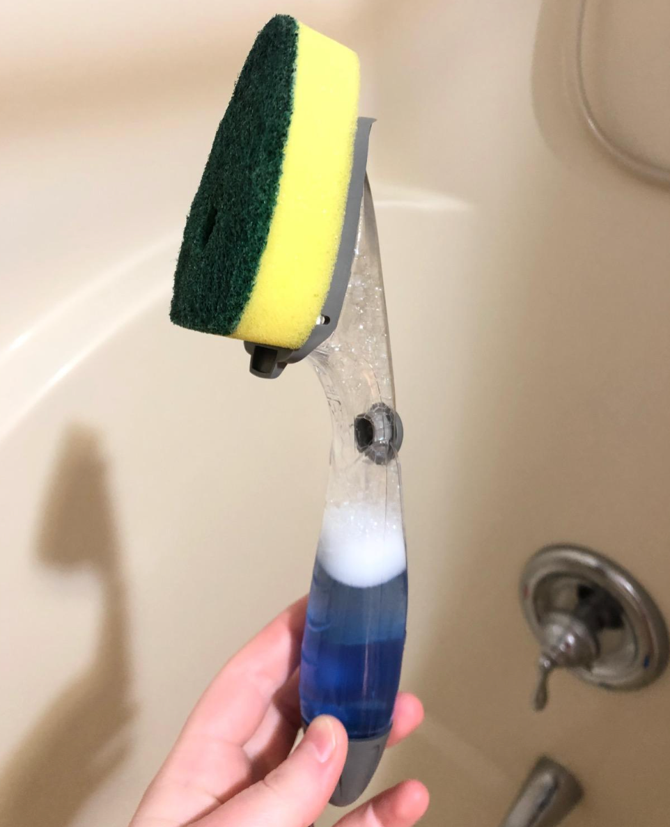 Reviewer holding up sponge attached to handle that has soap inside of it 