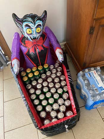 Inflatable vampire decoration holding assorted canned drinks successful  a bathtub-shaped instrumentality  adjacent  to a battalion  of bottled water