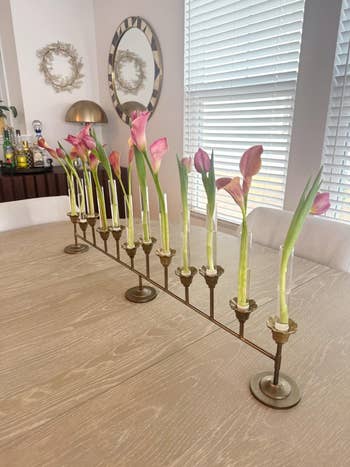 Calla lilies in a vintage, multi-holder brass vase on a wooden dining table, enhancing a cozy home setting