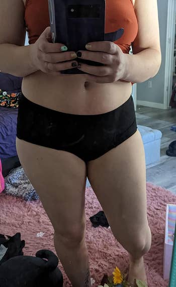 reviewer in period underwear, seen from waist to knees, taking a mirror selfie in a casual indoor setting