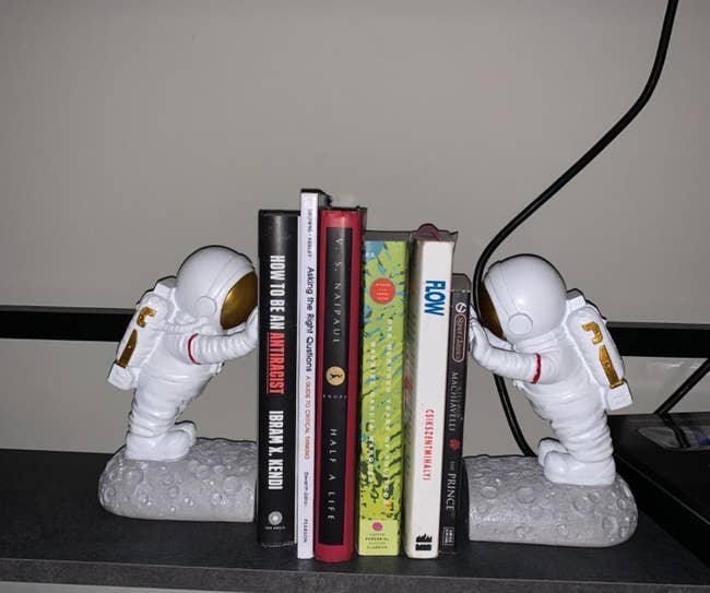 Two astronaut bookends holding a row of books on a shelf