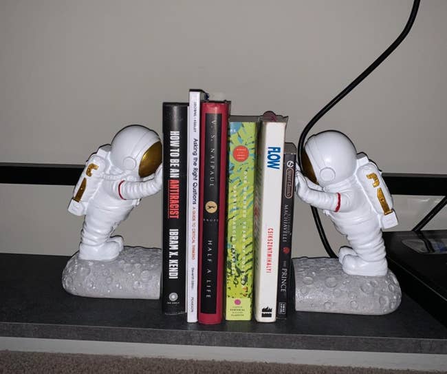 Two astronaut bookends holding a row of books on a shelf