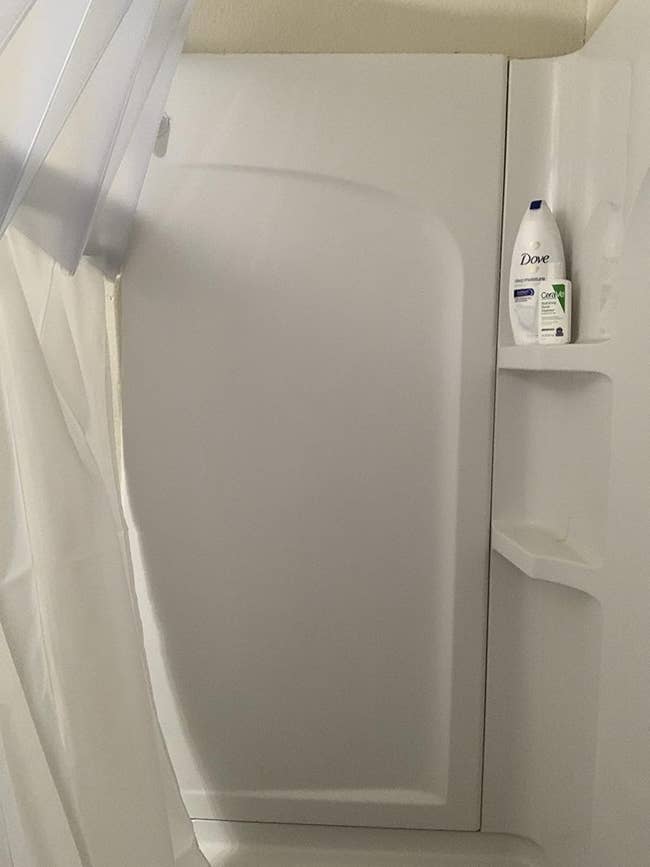 Shower with curtain partially unfastened and a vessel of Dove assemblage lavation connected a shelf