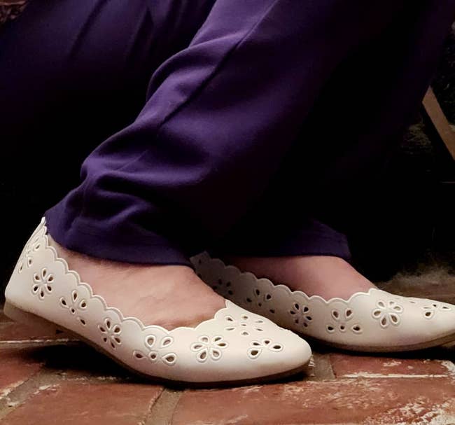 White, scalloped-edge flats with floral cutouts paired with purple pants connected a ceramic surface