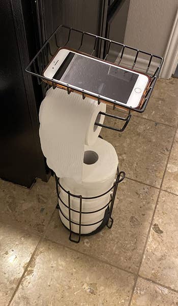 reviewer photo of the stocked toilet paper stand with a phone on the top shelf