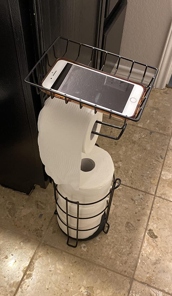 reviewer photo of the stocked toilet paper stand with a phone on the top shelf