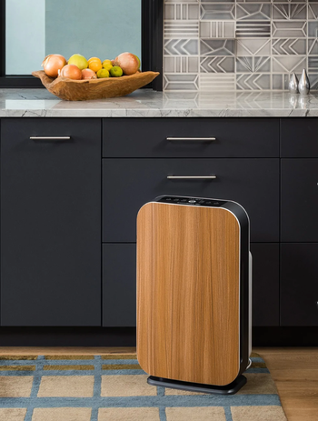 Wooden slim air purifier in front of black kitchen counter on grid carpet