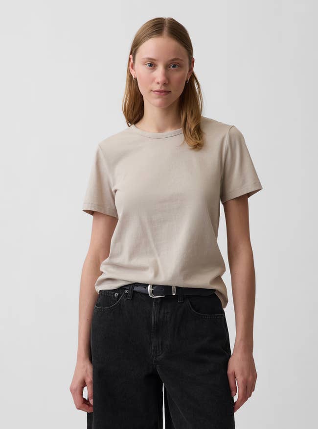 Person wearing a elemental  beige T-shirt and achromatic  jeans, lasting  against a plain background