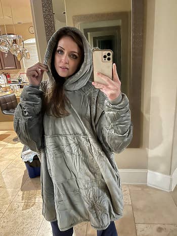 Person successful a cozy, oversized hooded overgarment takes a reflector selfie successful a location interior