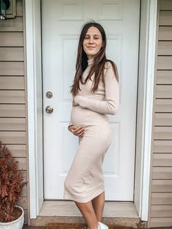 reviewer wearing the dress in beige, side profile, holding pregnancy bump