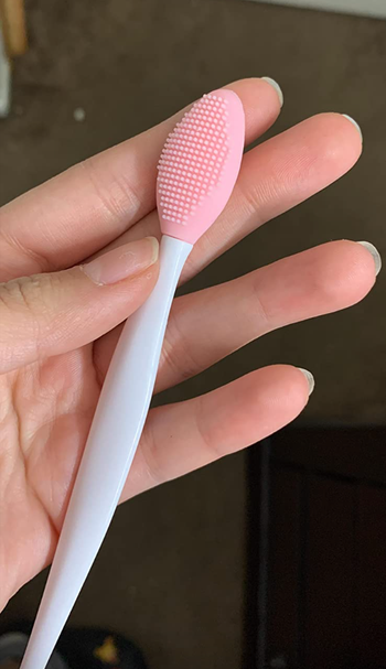 Reviewer holding pink silicone lightly bristled brush tool 