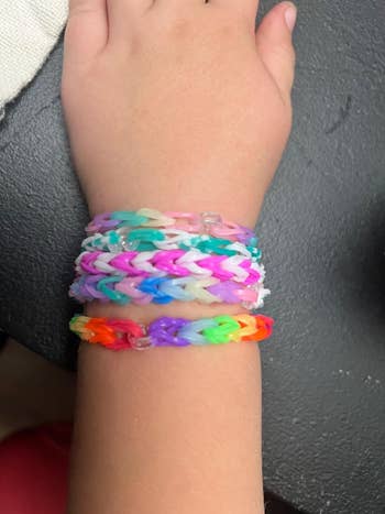 Child's wrist wearing colorful, woven rubber band bracelets in a textured pattern, displayed on a dark surface
