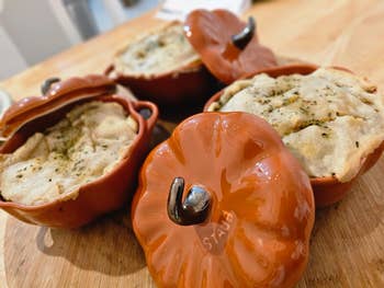 Three pumpkin-shaped ceramic dishes with savory pies and herbs on top