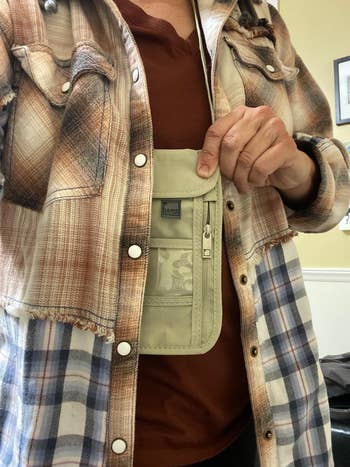 Person wearing a plaid shirt holds a small, beige travel pouch with a transparent pocket. Ideal for safely carrying essentials on trips