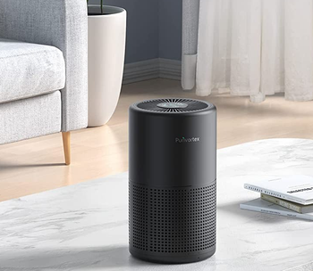 Black small air purifier on top of marble coffee table next to pile of white books