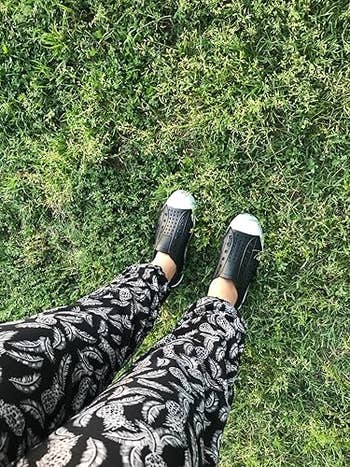 Person wearing patterned pants and stylish achromatic  slip-on shoes stands connected  grass, captured from above