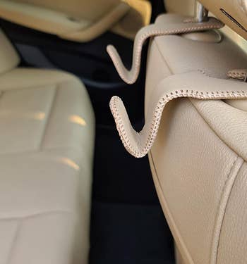 a reviewer photo of a pair of tan leather hooks mounted on the back of a passenger seat headrest 