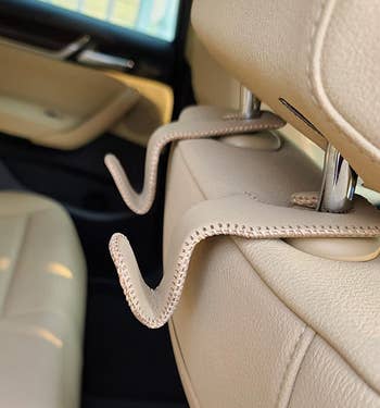 a reviewer photo of a pair of tan leather hooks mounted on the back of a passenger seat headrest 
