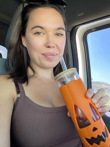 Woman successful a car holds a solid with a pumpkin look sleeve, implying a festive oregon seasonal buying theme