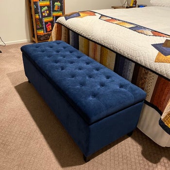 reviewer photo of the ottoman in navy blue at the foot of bed