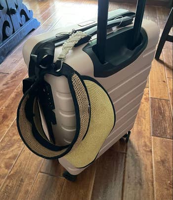 A suitcase with a chapeau  and a purse attached to its grip  sits connected  a woody  floor