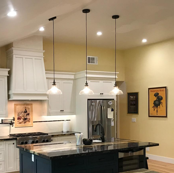 three pendant lights over black island counter in well-lit modern-looking kitchen